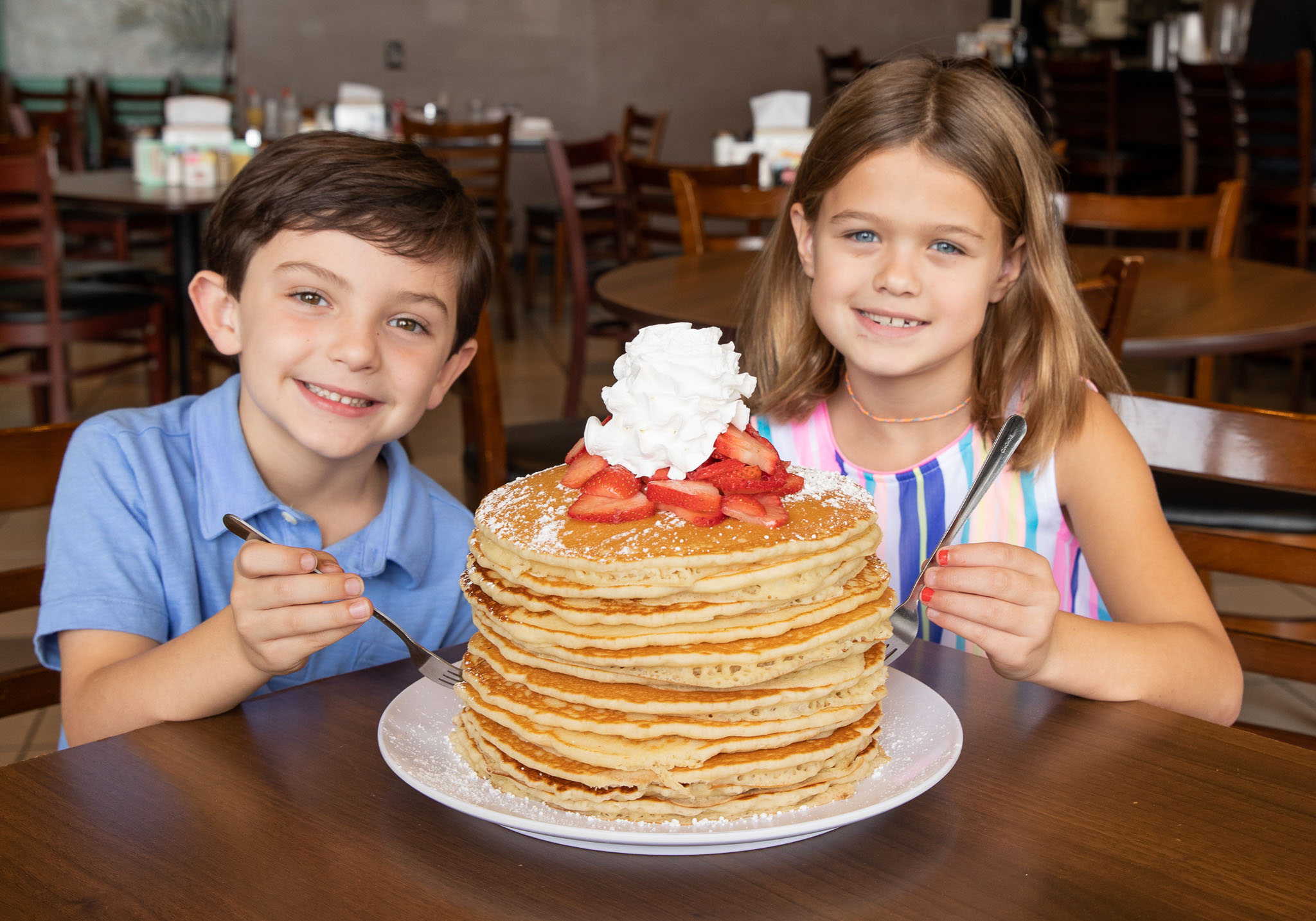 Kids smiling with a giant stack of pancakes at The Pancakery restaurant