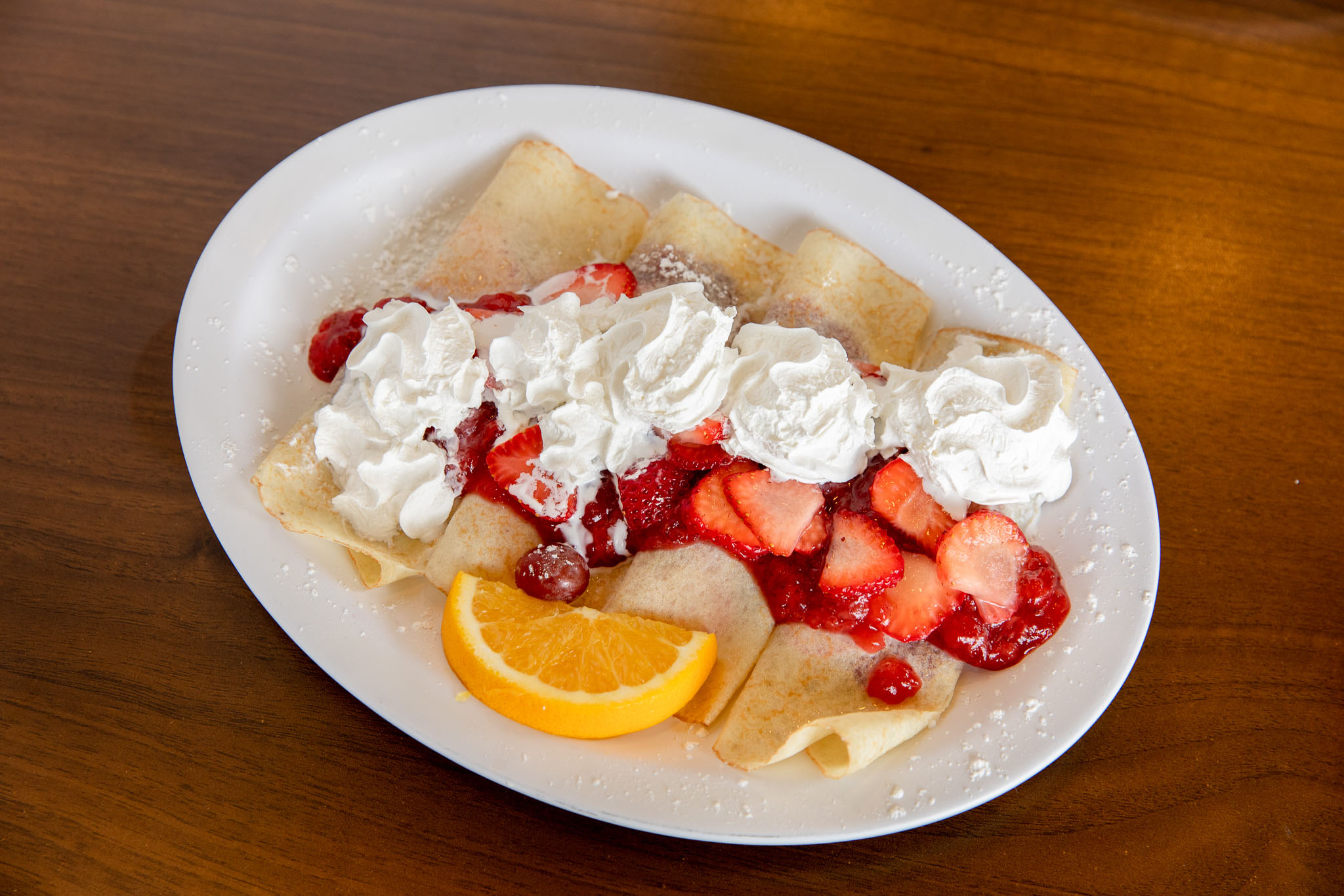 Fresh crepes topped with whipped cream, strawberries, and strawberry syrup