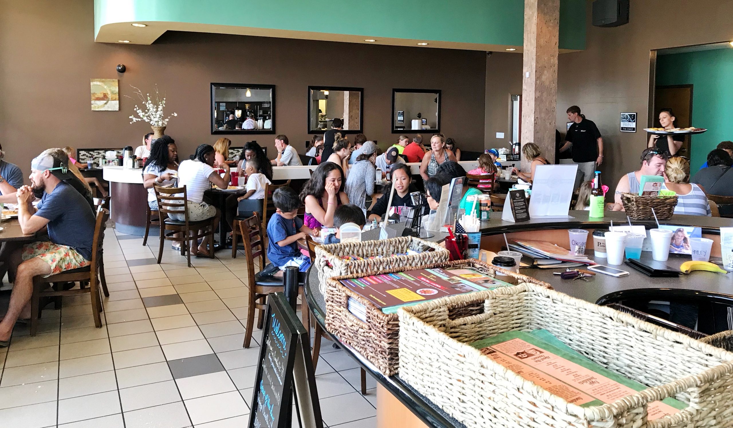 A bustling breakfast restaurant filled with diverse guests enjoying their meals at wooden tables.