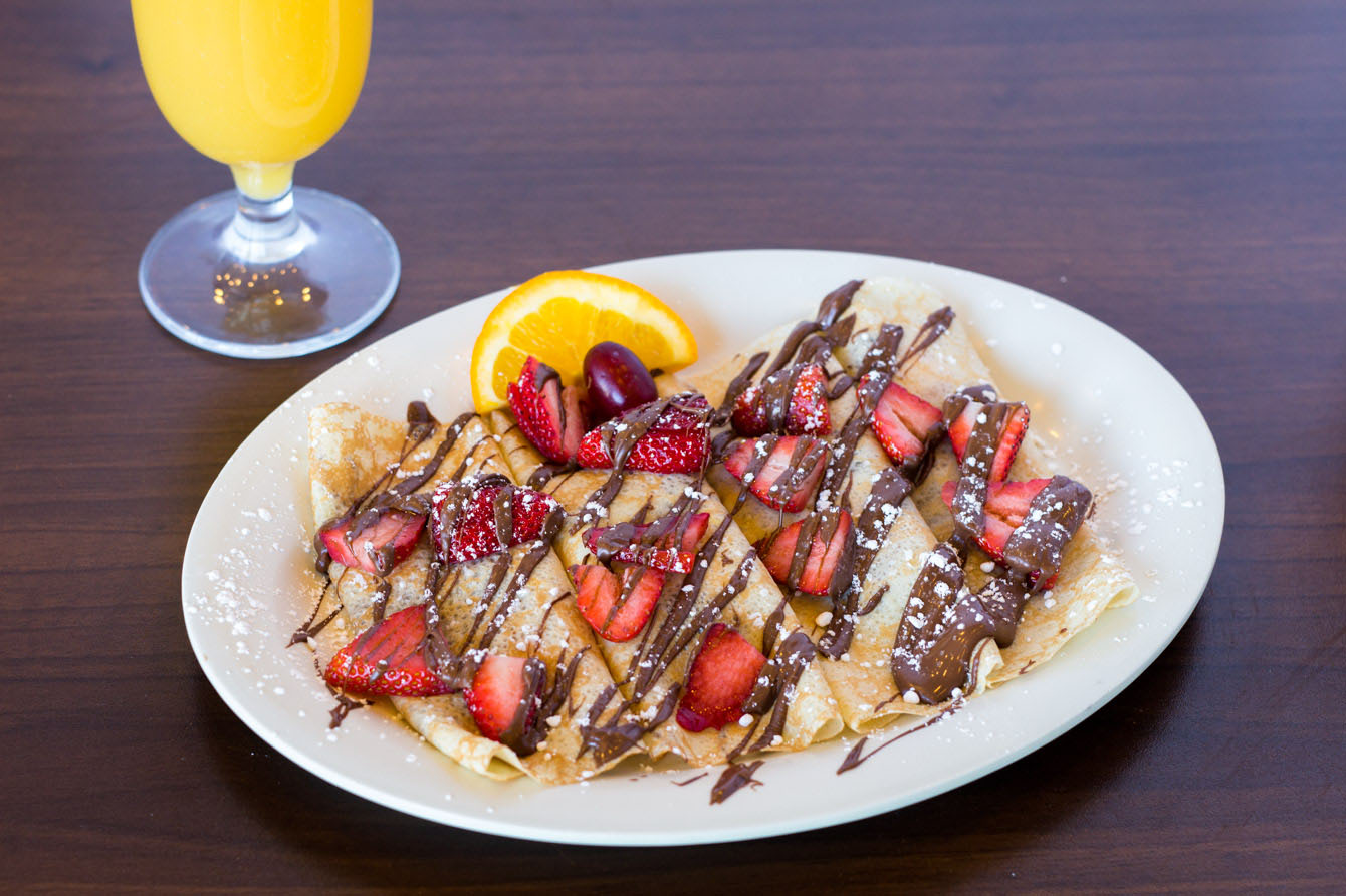 Thin crepes topped with sliced fresh strawberries, drizzled with chocolate syrup