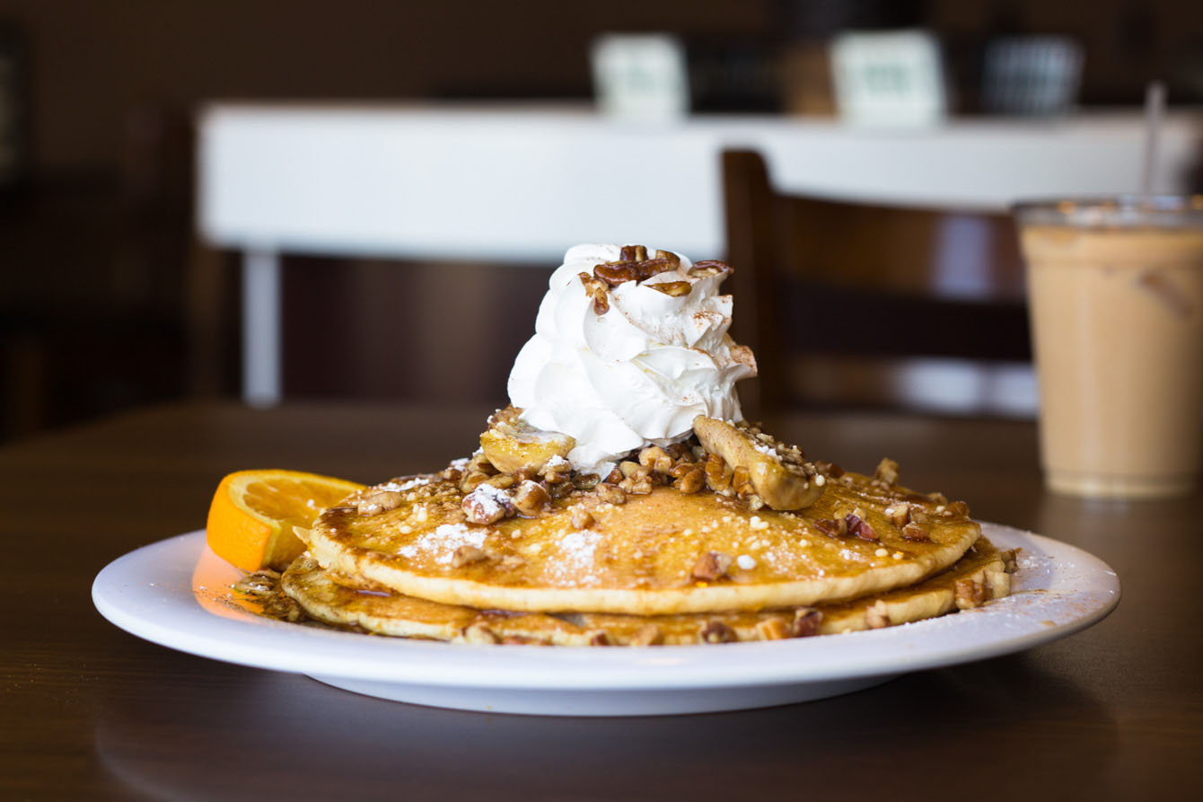 A tall stack of fluffy pancakes topped with caramelized banana slices, chopped pecans